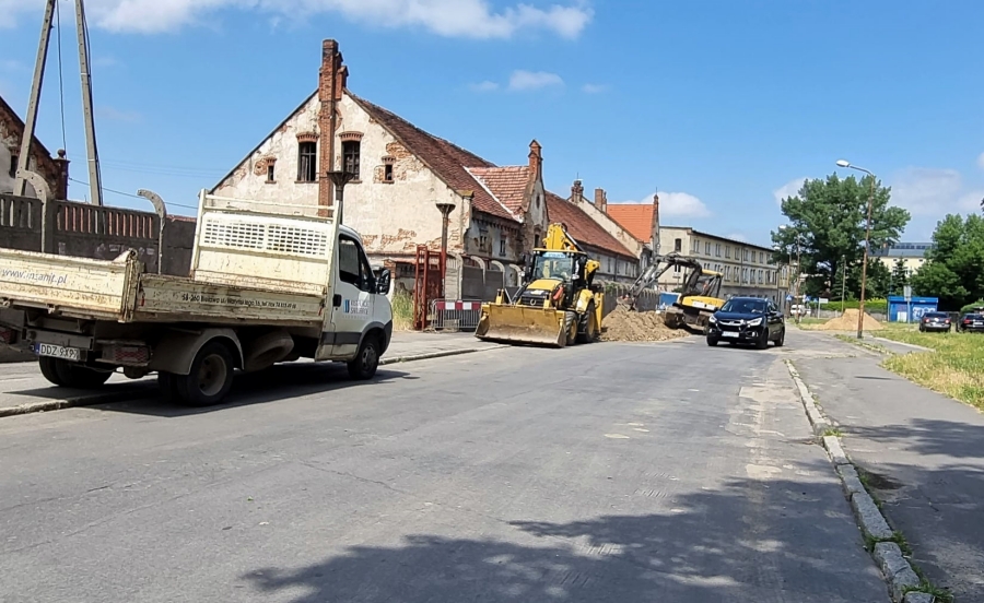 Na zdjęciu sprzęt remontowy - spychacz, samochód z przyczepą na materiały budowlane przy przebudowywanej części ulic. Po lewej stronie mocno zniszczone zabudowania